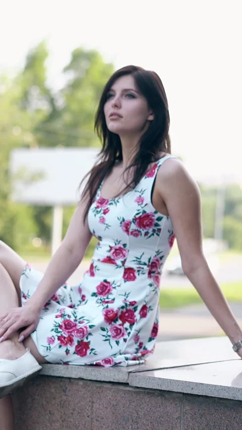 Round motion long haired brunette girl sits on grey parapet Vidéo 308002601