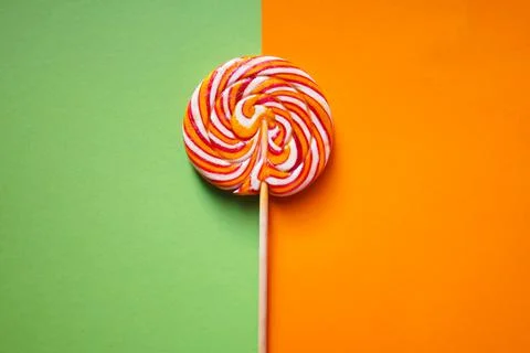 Round multi-colored lollipop on a two-tone background. Green and orange. Stock Photos