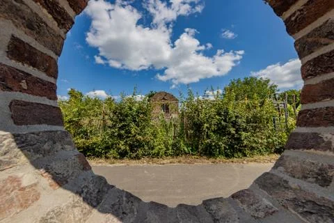 Round opening in a brick wall looking through it at a dilapidated building Stock Photos