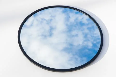 A round or oval mirror with a reflection of the blue sky and white clouds. Close Stock Photos