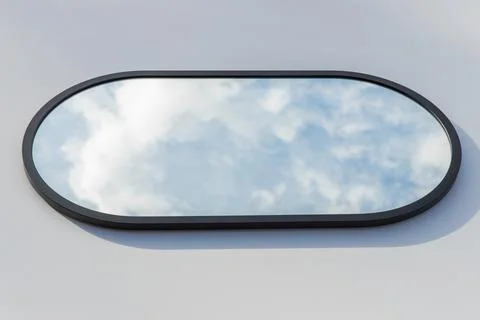 A round or oval mirror with a reflection of the blue sky and white clouds. Close Stock Photos
