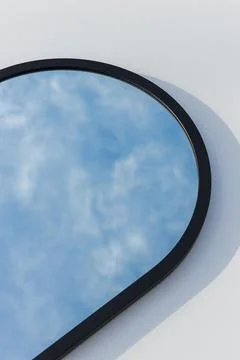 A round or oval mirror with a reflection of the blue sky and white clouds. Close Stock Photos