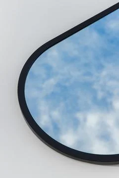 A round or oval mirror with a reflection of the blue sky and white clouds. Close Stock Photos