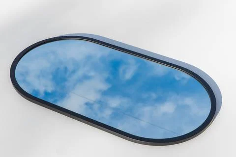 A round or oval mirror with a reflection of the blue sky and white clouds. Close Stock Photos