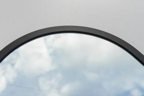 A round or oval mirror with a reflection of the blue sky and white clouds. Close Foto stock