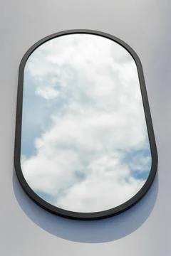 A round or oval mirror with a reflection of the blue sky and white clouds. Close Stock Photos