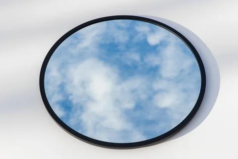 A round or oval mirror with a reflection of the blue sky and white clouds. Close Stock Photos