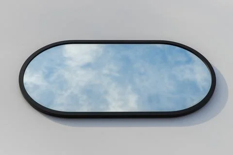A round or oval mirror with a reflection of the blue sky and white clouds. Close Stock Photos