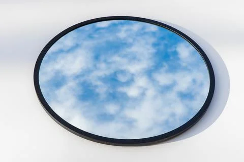 A round or oval mirror with a reflection of the blue sky and white clouds. Close Foto stock