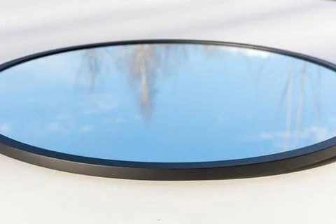 A round or oval mirror with a reflection of the blue sky and white clouds. Close Stock Photos