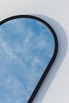 A round or oval mirror with a reflection of the blue sky and white clouds. Close Stock Photos