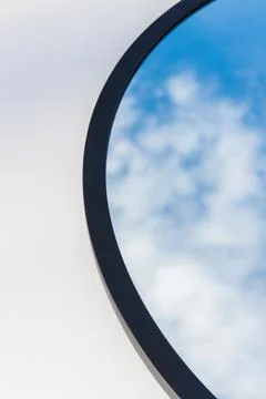 A round or oval mirror with a reflection of the blue sky and white clouds. Close Stock Photos