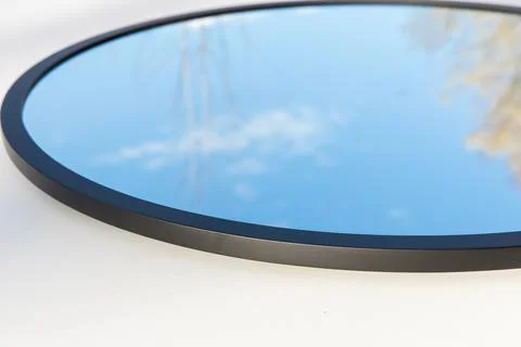 A round or oval mirror with a reflection of the blue sky and white clouds. Close Foto stock