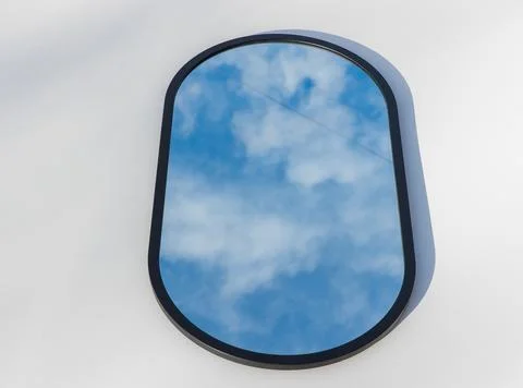 A round or oval mirror with a reflection of the blue sky and white clouds. Close Stock Photos