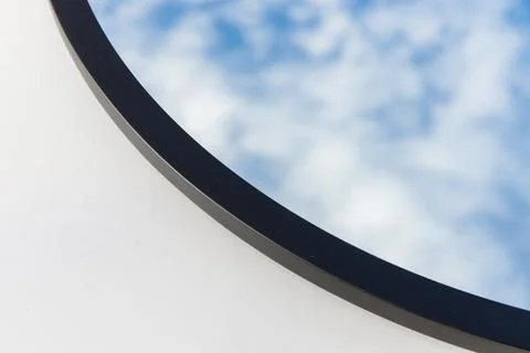 A round or oval mirror with a reflection of the blue sky and white clouds. Close Stock Photos