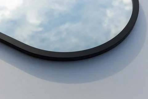 A round or oval mirror with a reflection of the blue sky and white clouds. Close Stock Photos