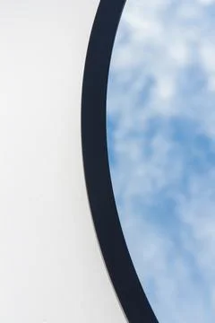 A round or oval mirror with a reflection of the blue sky and white clouds. Close Stock Photos