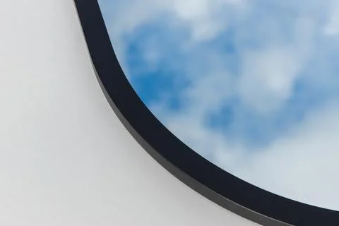 A round or oval mirror with a reflection of the blue sky and white clouds. Close Stock Photos