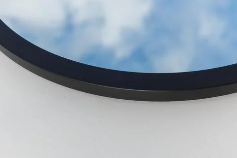 A round or oval mirror with a reflection of the blue sky and white clouds. Close Stock Photos