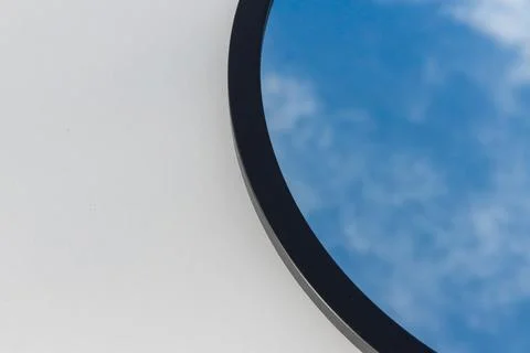 A round or oval mirror with a reflection of the blue sky and white clouds. Close Stock Photos