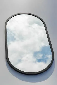 A round or oval mirror with a reflection of the blue sky and white clouds. Close Stock Photos