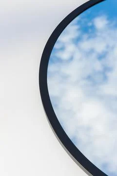 A round or oval mirror with a reflection of the blue sky and white clouds. Close Stock Photos