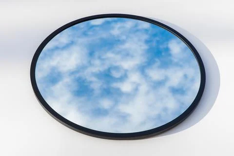 A round or oval mirror with a reflection of the blue sky and white clouds. Close Stock Photos