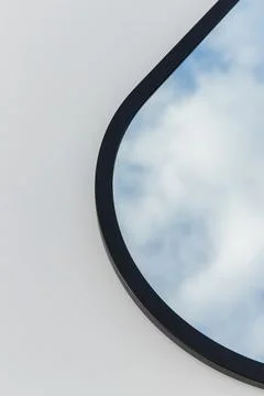 A round or oval mirror with a reflection of the blue sky and white clouds. Close Stock Photos