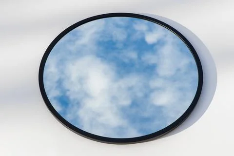 A round or oval mirror with a reflection of the blue sky and white clouds. Close Stock Photos
