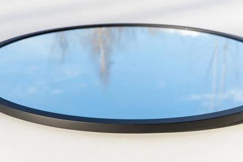 A round or oval mirror with a reflection of the blue sky and white clouds. Close Foto stock