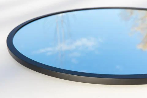 A round or oval mirror with a reflection of the blue sky and white clouds. Close Stock Photos