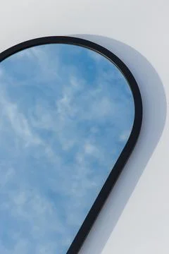 A round or oval mirror with a reflection of the blue sky and white clouds. Close Stock Photos
