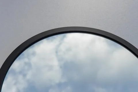 A round or oval mirror with a reflection of the blue sky and white clouds. Close Stock Photos