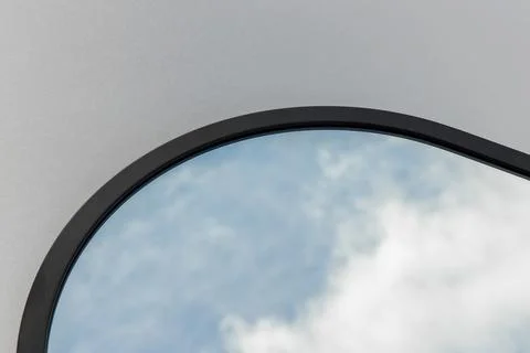 A round or oval mirror with a reflection of the blue sky and white clouds. Close Stock Photos
