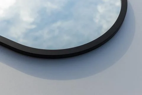 A round or oval mirror with a reflection of the blue sky and white clouds. Close Stock Photos