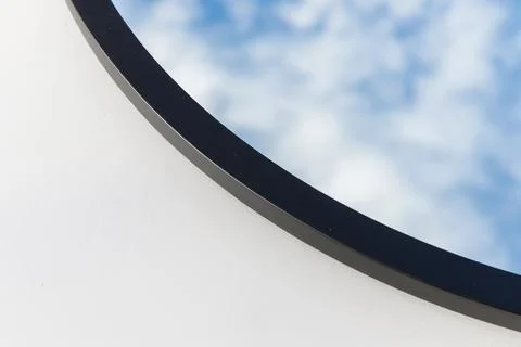A round or oval mirror with a reflection of the blue sky and white clouds. Close Stock Photos