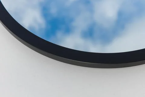 A round or oval mirror with a reflection of the blue sky and white clouds. Close Stock Photos