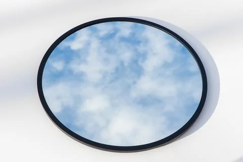 A round or oval mirror with a reflection of the blue sky and white clouds. Close Stock Photos