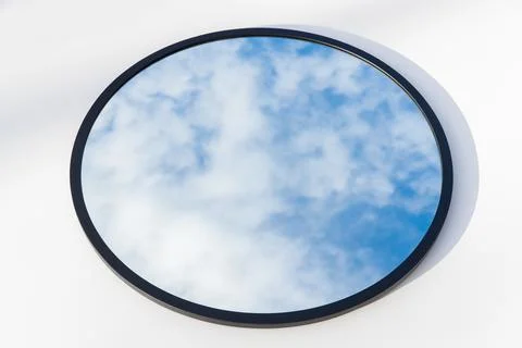 A round or oval mirror with a reflection of the blue sky and white clouds. Close Stock Photos