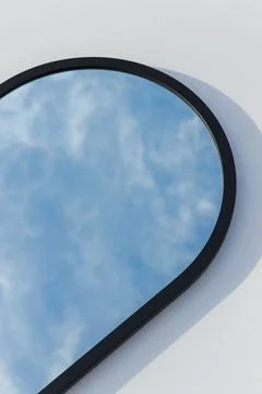 A round or oval mirror with a reflection of the blue sky and white clouds. Close Stock Photos