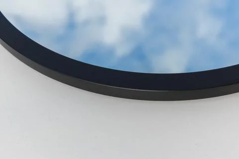 A round or oval mirror with a reflection of the blue sky and white clouds. Close Stock Photos