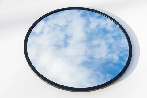 A round or oval mirror with a reflection of the blue sky and white clouds. Close Stock Photos