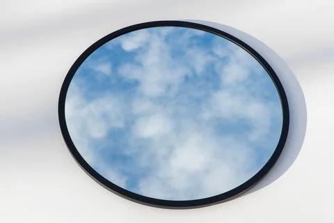 A round or oval mirror with a reflection of the blue sky and white clouds. Close Stock Photos