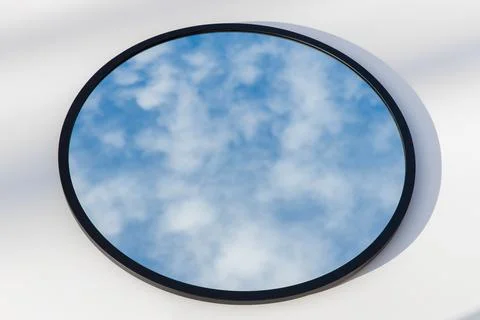 A round or oval mirror with a reflection of the blue sky and white clouds. Close Stock Photos