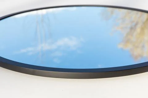 A round or oval mirror with a reflection of the blue sky and white clouds. Close Stock Photos