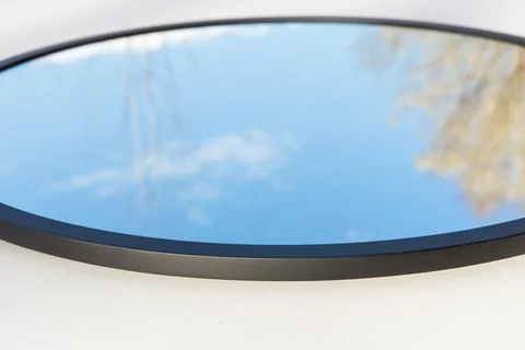 A round or oval mirror with a reflection of the blue sky and white clouds. Close Stock Photos