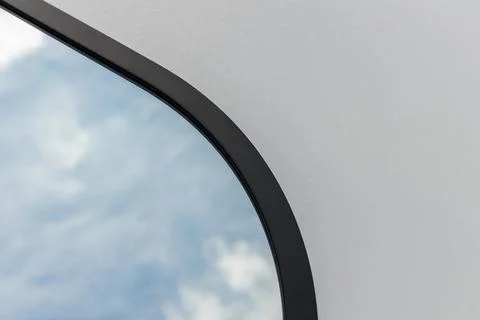 A round or oval mirror with a reflection of the blue sky and white clouds. Close Stock-Fotos