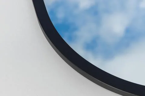 A round or oval mirror with a reflection of the blue sky and white clouds. Close Stock Photos