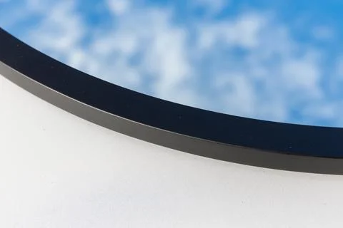 A round or oval mirror with a reflection of the blue sky and white clouds. Close Foto stock