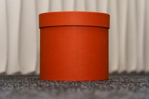 Round orange box placed on a textured surface in a simple indoor setting Foto stock